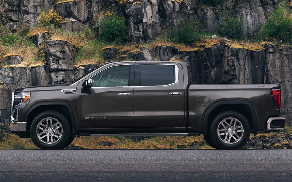Sideview of brown Sierra 1500 in front of rocky outcrop